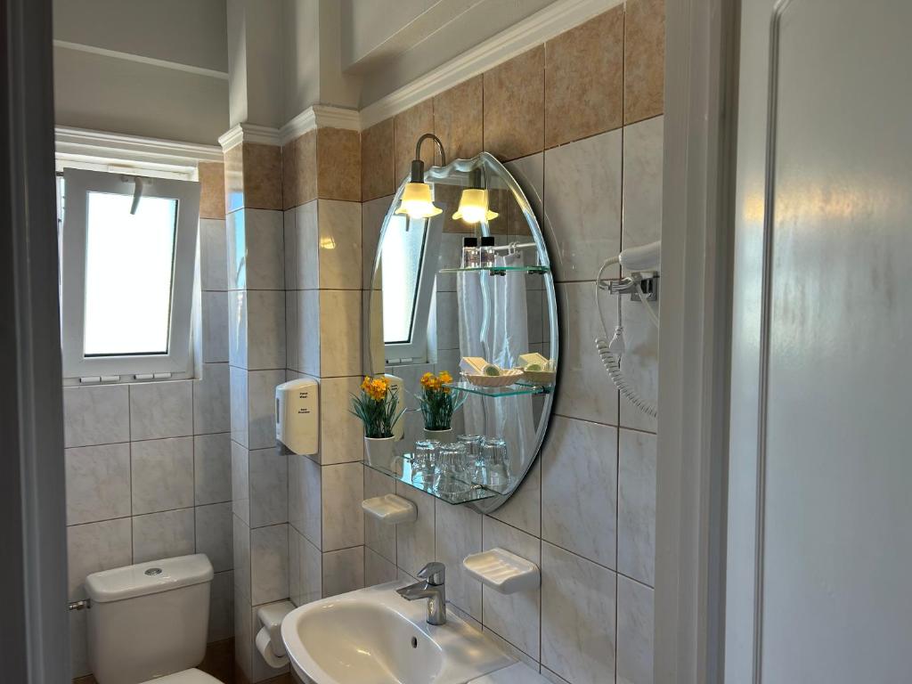 Mūsdienīgs vannas istabas interjers ar spoguli, higiēnas līdzekļiem un ziediem uz plaukta. Izgaismota telpa ar flīzēm un logiem.