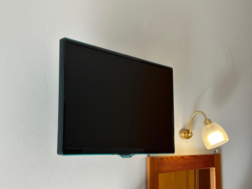 Mūsdienīgs plakanas ekrāna televizors pie sienas, blakus gaismas ķermenim un spogulim.