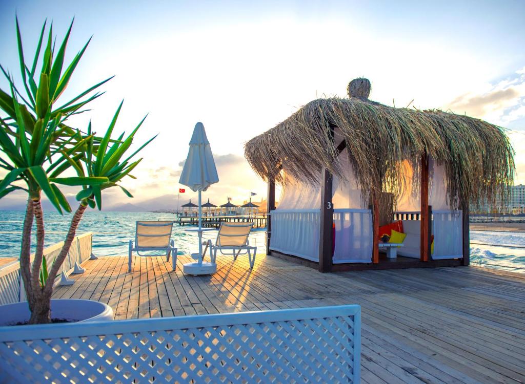 Koka paviljons pie Liberty Hotels Lara pludmalē, ar sauļošanās krēsliem un jūru fonā.