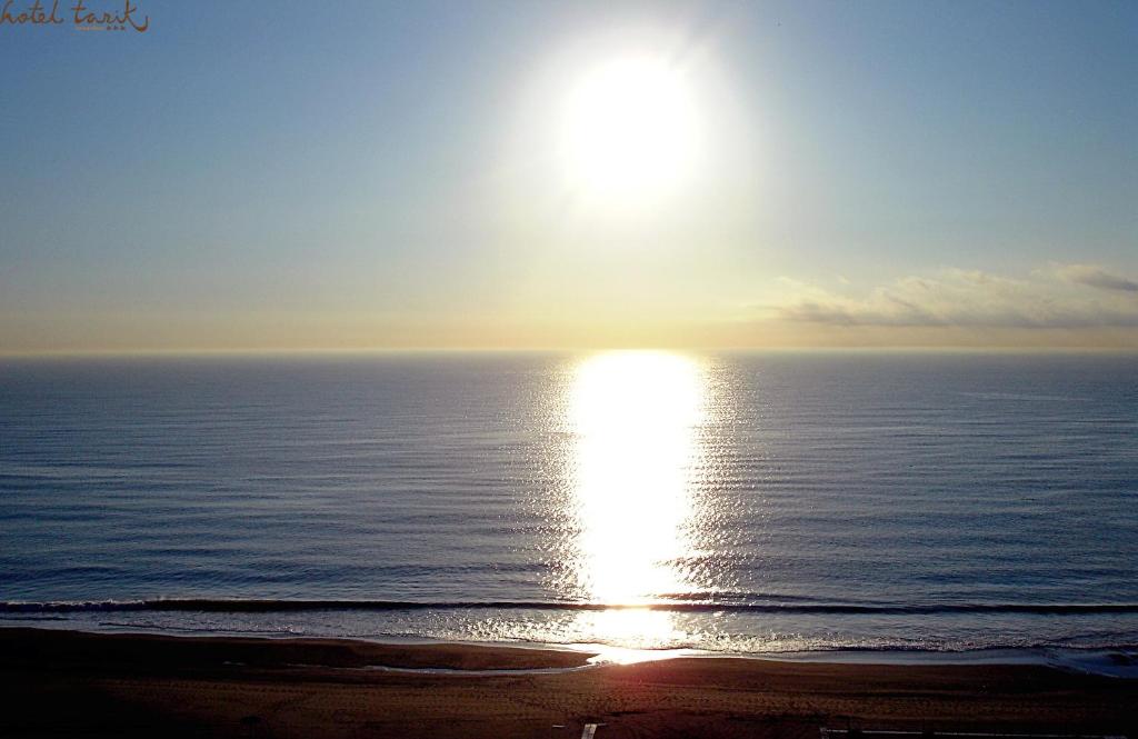 Saulriets pār mierīgu jūru, atspoguļojot saules gaismu uz ūdens virsmas. Skats veido mierīgu un relaksējošu atmosfēru, ideāli piemērots pludmales brīvdienām.