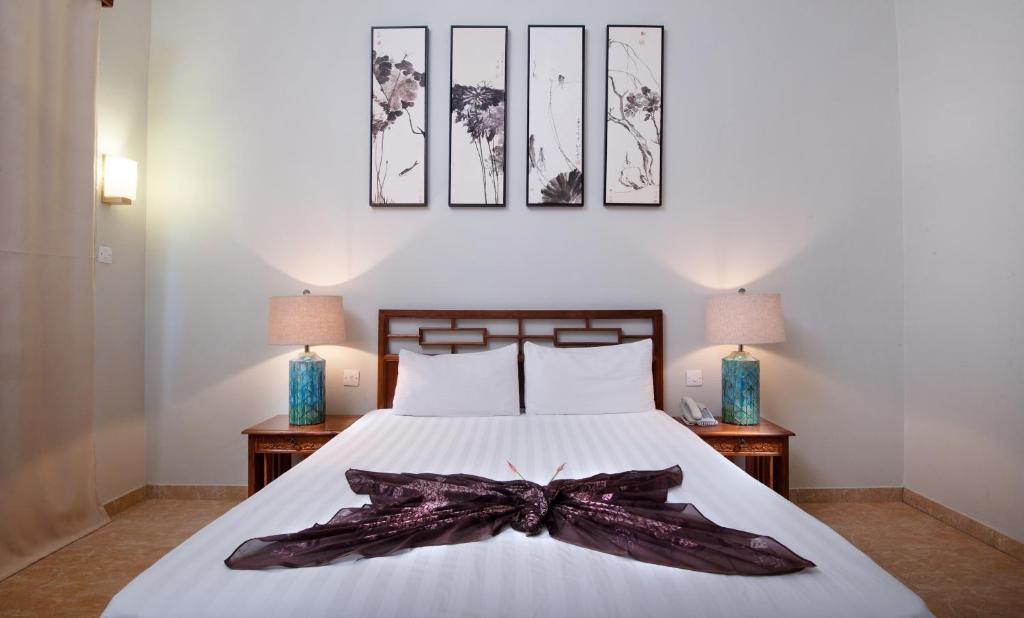 Mūsdienīga guļamistaba ar baltu gultu un dekoratīvu pārklāju, papildināta ar mākslas darbiem uz sienas un stilīgām lampām. Interjers ir gaišs un elegants, radot komfortu un relaksāciju.