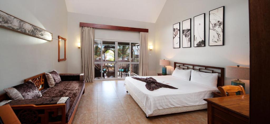 Moderns viesnīcas numurs ar plašu gultu, stūra dīvānu un logiem, kas ved uz āra terasi. Interjērā ir eleganta dekorācija un mākslas darbi uz sienām.