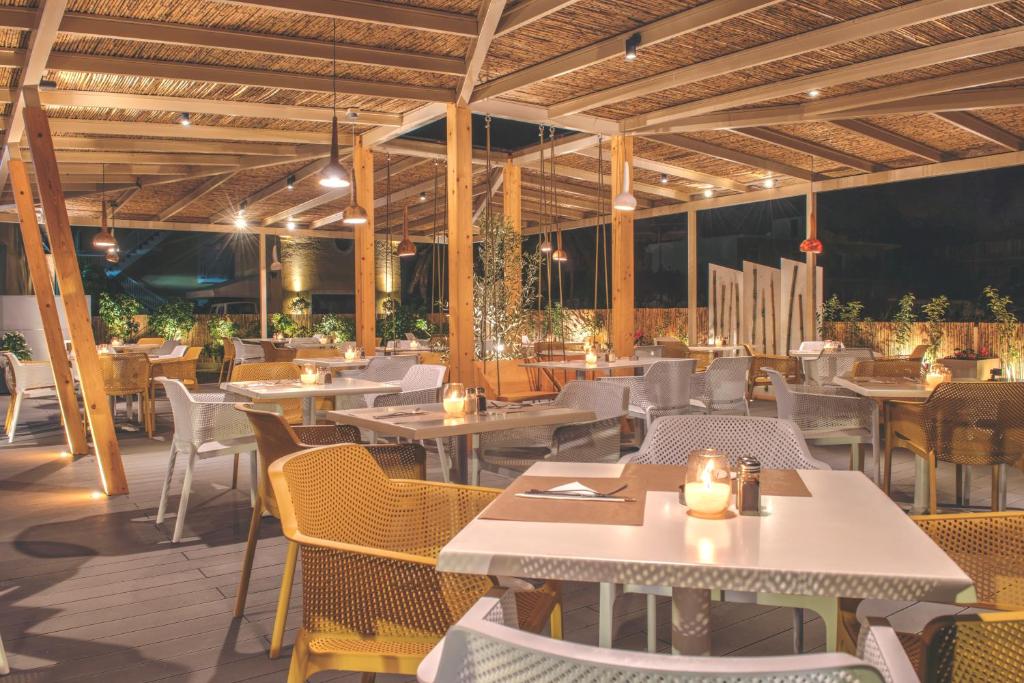 Moderns restorāns ar atvērtu terasi, kas apgaismota ar siltu gaismu. Galdi ir klāti ar sveču gaismu, radot intīmu atmosfēru.
