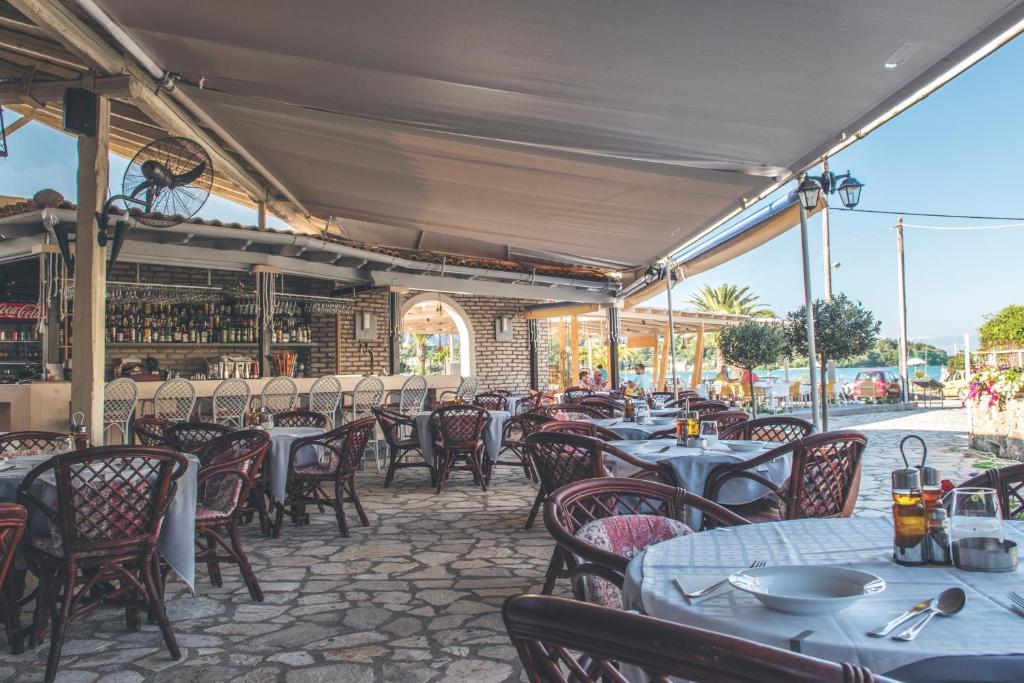 Skaistas restorāna terases skats ar rattan krēsliem un galdiem, kas izvietoti zem jumta. Fons ietver bāru ar dzērieniem un skatu uz jūru.