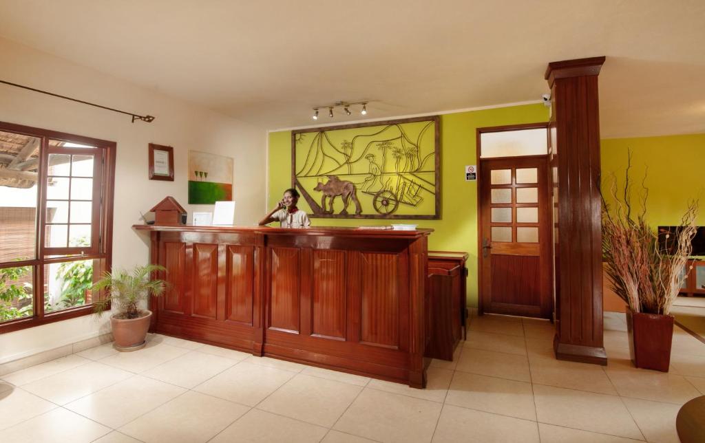 Recepcija ar koka letēm un krāsainu sienu apdari, kur strādā darbinieks. Telpā ir logs un dekoratīvi augi.