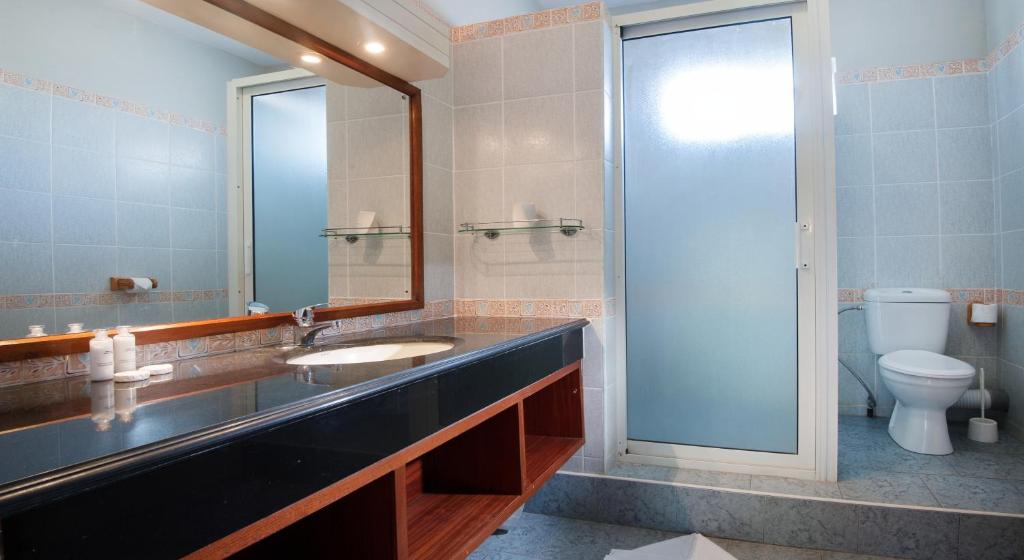 Mūsdienīgs vannas istabas interjers ar melnu izlietni, spoguli un stikla dušas kabīni. Gaišas flīzes un koka akcenti rada elegantu atmosfēru.