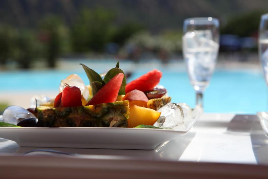 Svaigu augļu salāti ar ananāsu, arbūzu un citiem augļiem, pasniegti blakus baseinam. Ideāla uzkoda atpūtai saulainā dienā.