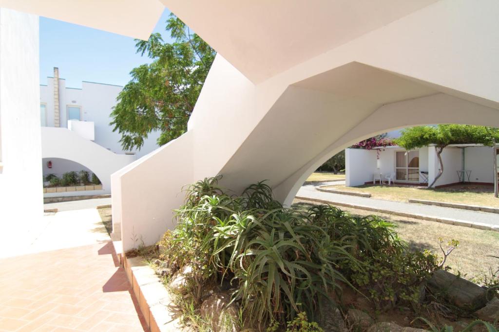 Mūsdienīga arhitektūra ar baltiem mūriem un dārzu, kas redzams caur izliektu arku. Gaisīgs un gaišs pagalms ar zāli un augiem.