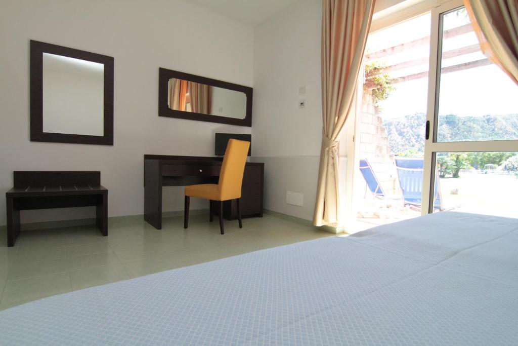 Mūsdienīga viesnīcas numura interjers ar rakstāmgaldu, krēslu un spoguli, kas atveras uz balkonu ar skatu uz dārzu.