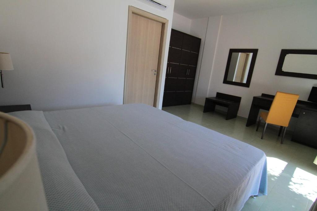 Mūsdienīgs guļamistabas interjers ar plašu gultu, melnu drēbju skapi un rakstāmgaldu ar dzeltenu krēslu. Telpa ir gaiša un minimālistiska, radot mierīgu atmosfēru.