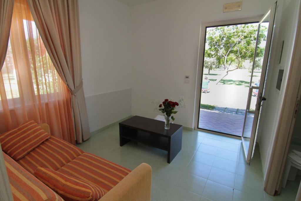 Mūsdienīga viesistaba ar dīvānu un galdu, caur atvērtiem durvīm redzama zaļā teritorija. Iekārtojums ir gaišs un viesmīlīgs.