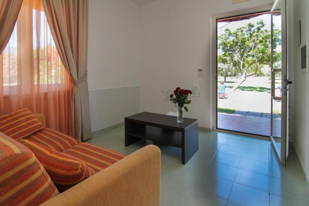 Mūsdienīgs un gaišs viesistabas interjers ar dīvānu, kafijas galdiņu un logiem, caur kuriem redzams apzaļumots āra skats.