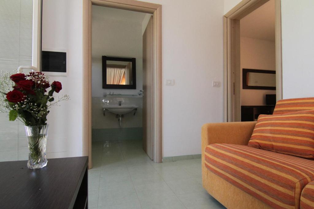 Mājīgā telpā ar dīvānu un ziedu kompozīciju, redzams ieejas ceļš uz vannas istabu. Gaisma ienāk no loga, radot patīkamu atmosfēru.