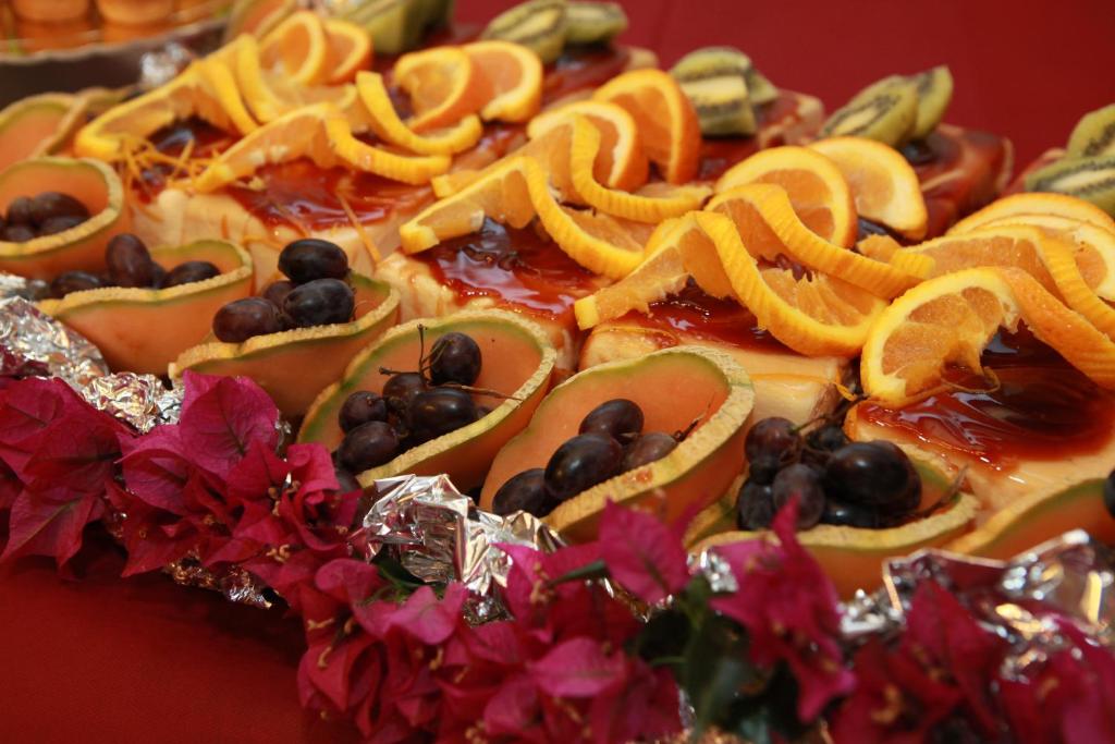 Svaigu augļu un dekoratīvu ziedu kompozīcija, kas ietver apelsīnus, kiwī un melones, rotāta ar sarkanām zieda lapām.