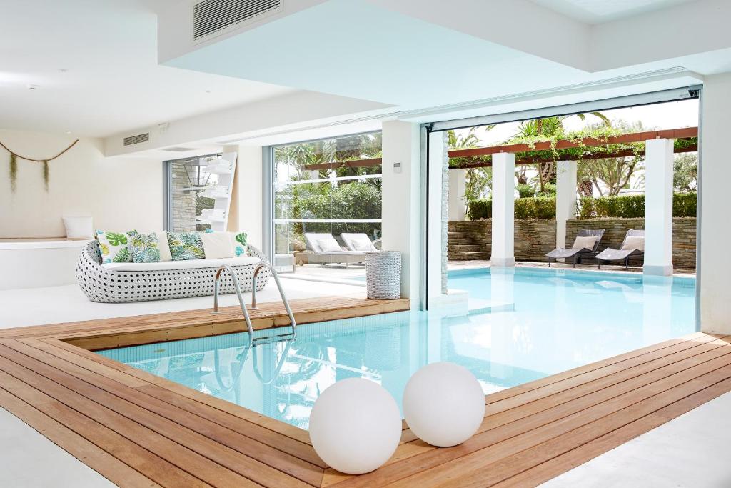 Mūsdienīgs iekštelpu baseins ar koka terasi, stilīgu dīvānu un daudzām saulainām vietām atpūtai. Plašs logs nodrošina gaišumu un skatu uz ārējo dārzu.