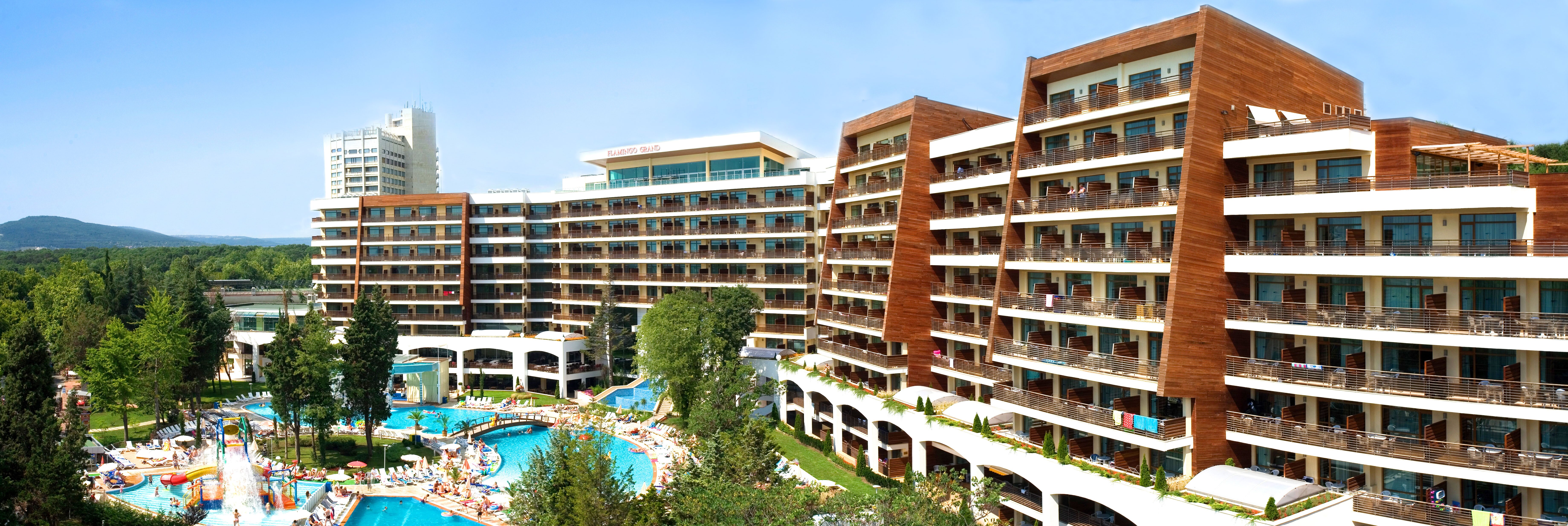 Viesnīcas komplekss ar modernu arhitektūru un baseinu, kas ieskauts zaļā vidē. Viesnīcas teritorijā ir ūdens atrakciju parks un atpūtas zonas. panoramic view with beach and pools