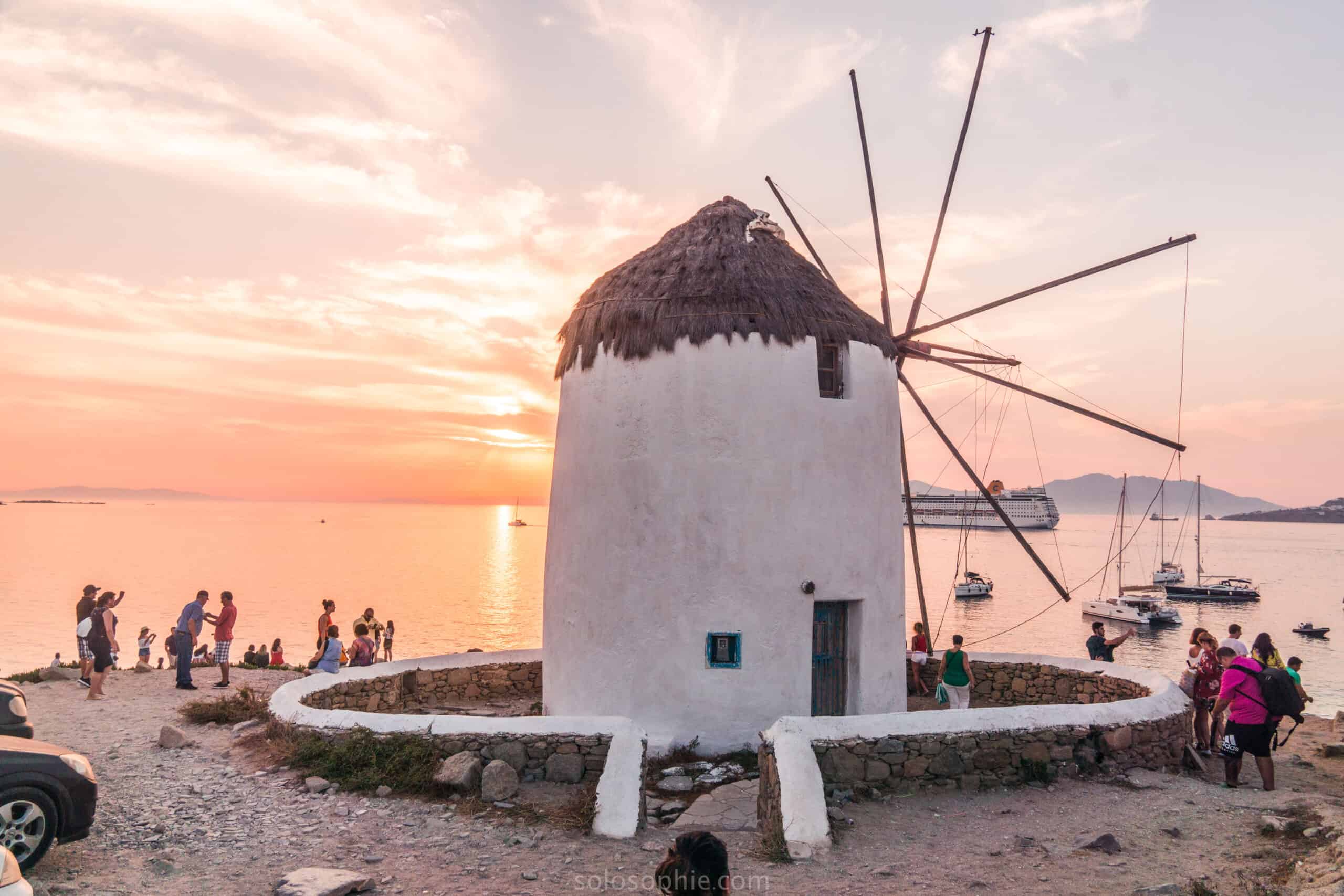 Mikonos vējdzirnavas saulrietā - balti nami un jūras piekrastes skats Vanilla Travel kruīzā