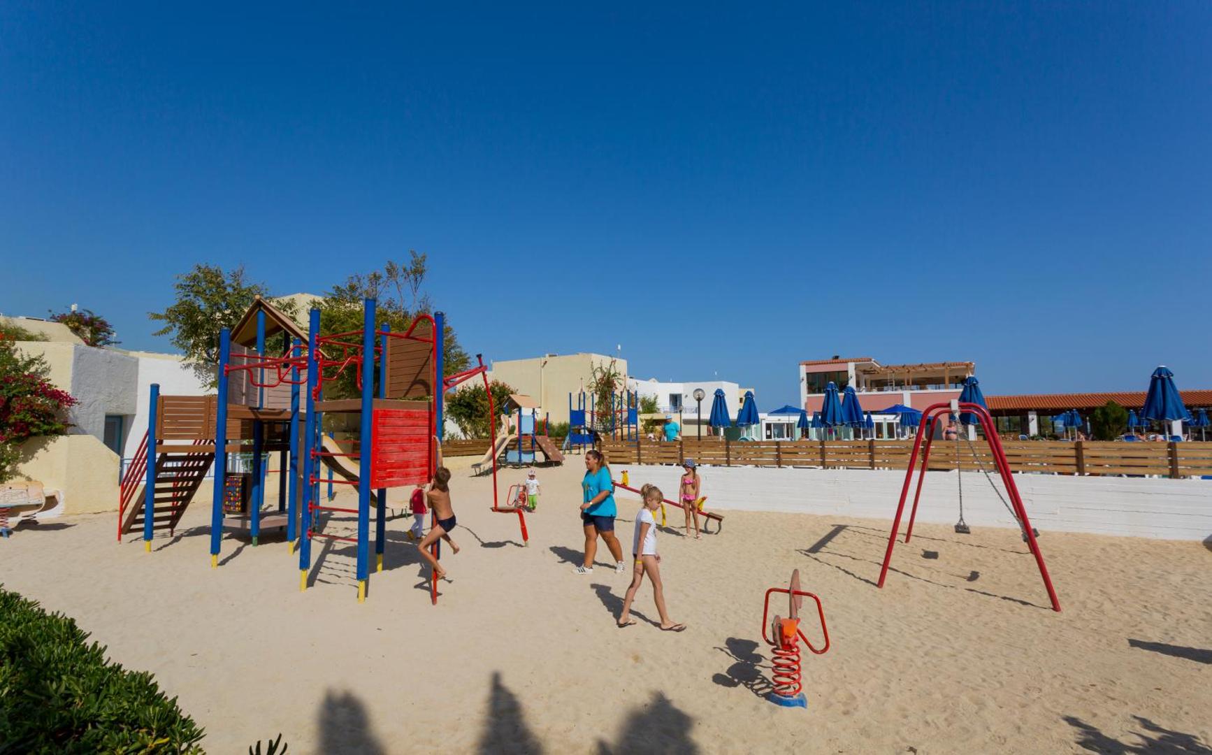 Dessole Malia Beach bērnu rotaļu laukums smiltīs ar slidkalniņiem un šūpolēm Krētas piekrastē zem skaidrām debesīm