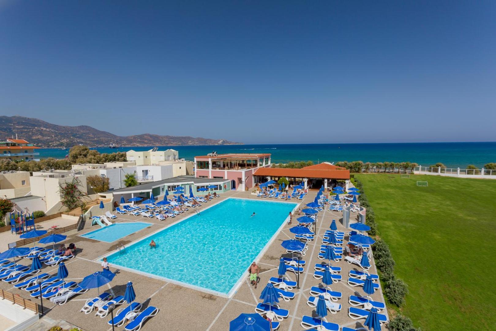 Skats no augšas uz Dessole Malia Beach baseinu un blakus esošo pludmali — zils ūdens, sauļošanās zona un plašs zāliens pie jūras