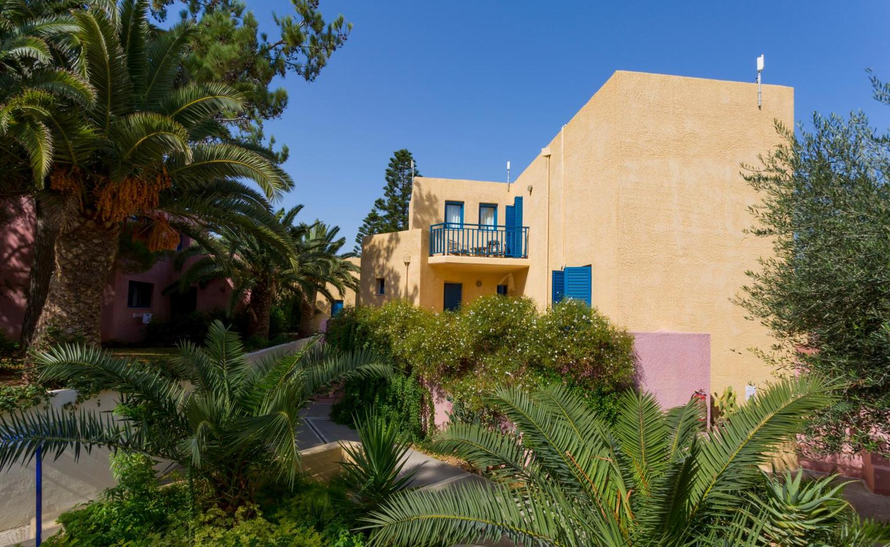 Dessole Malia Beach bungalo stila numuri ar balkoniem, ko ieskauj palmas un ziedoši krūmi dārzā