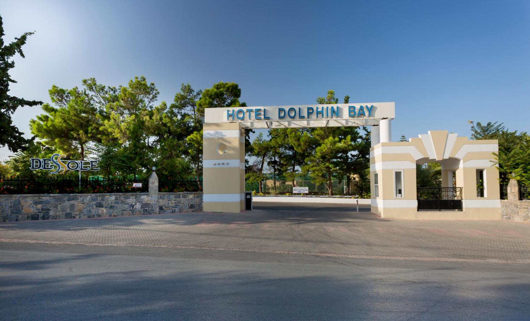 Dessole Malia Beach (Dolphin Bay) iebrauktuves vārti ar viesnīcas nosaukumu, ko ieskauj zaļi koki un akmens mūris