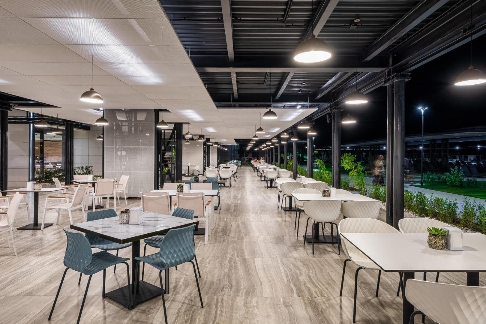 Voya Beach Resort āra terases restorāns vakarā ar modernām mēbelēm, apgaismojumu un skatu uz dārzu