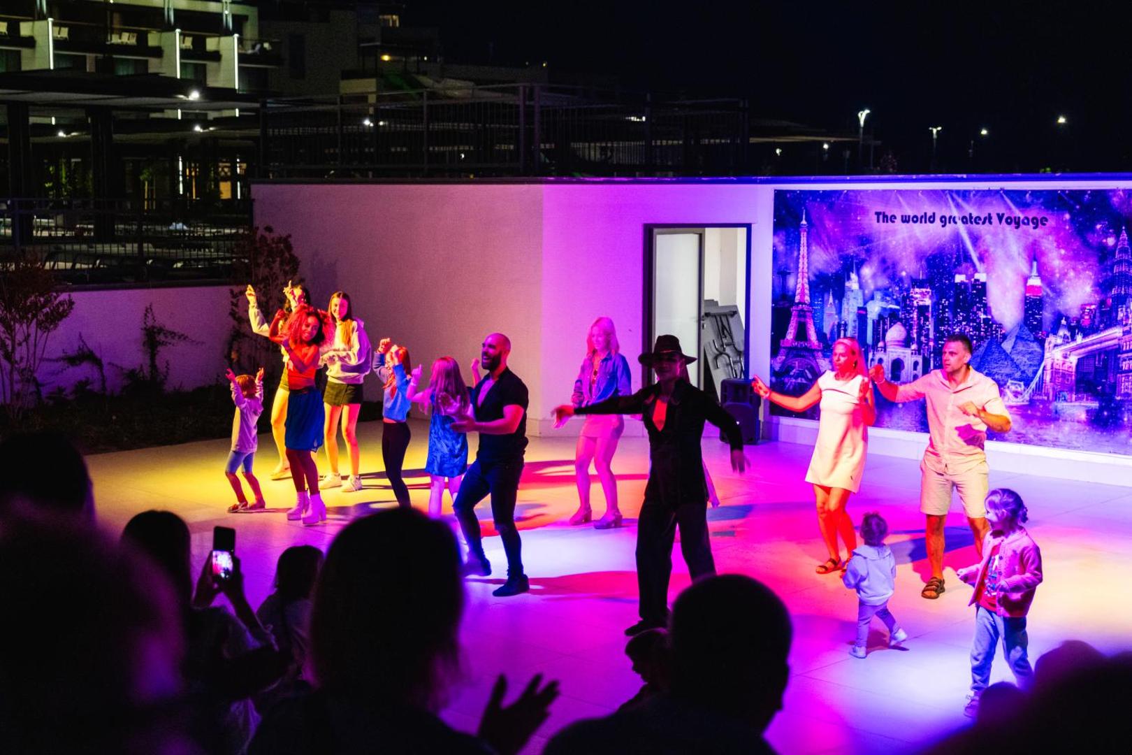 Vakara izklaides programma Voya Beach Resort — viesi un animatori dejo uz izgaismotas skatuves krāsainu gaismu pavadībā