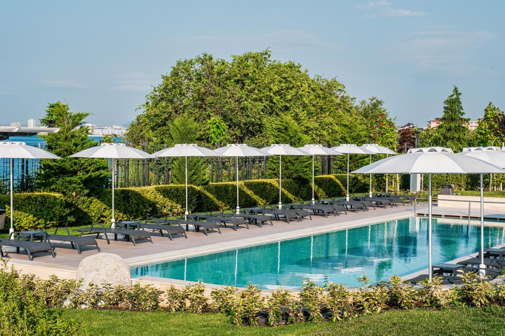 Voya Beach Resort āra baseins ar saulessargiem un zviļņiem, ko ieskauj kopti apstādījumi un skats uz Melno jūru.