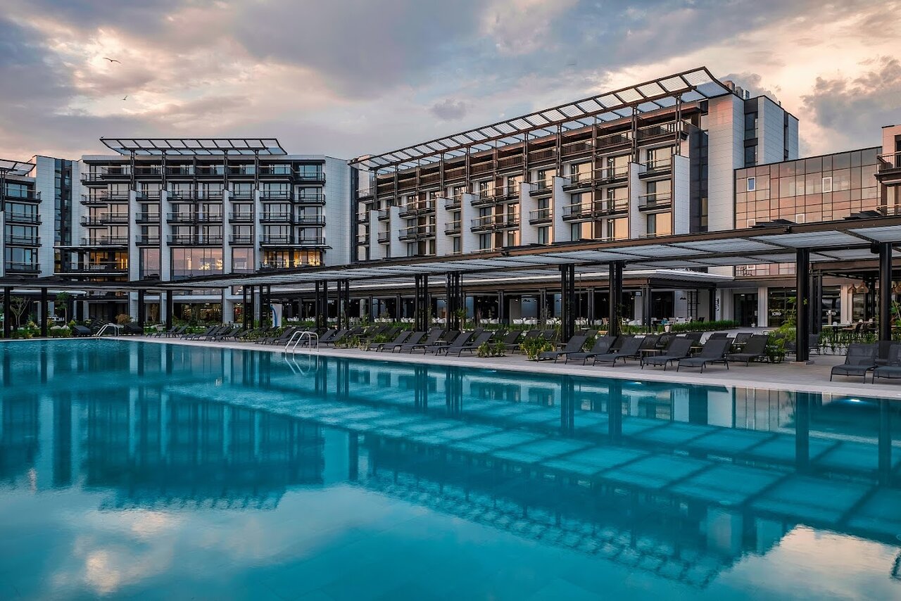 Voya Beach Resort modernā arhitektūra un lielais āra baseins saulrietā Sveti Vlasā, Bulgārijā, ar atpūtas krēsliem un terasi.