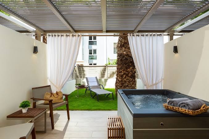 Theartemis Palace numurs ar privātu terasi un džakuzi Retimno, Krētā — atpūtas zona ar zālāju, sauļošanās krēslu un modernu dizainu