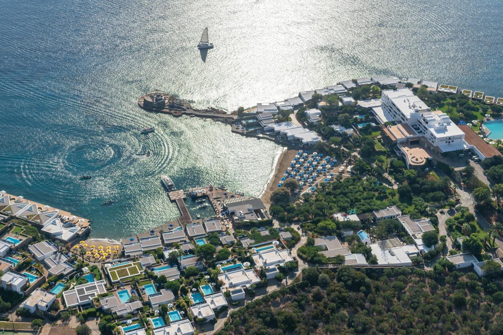 Aerofoto skats uz Elounda Beach Hotel And Villas kompleksu, baltajiem bungalo ar privātiem baseiniem un jahtu piestātni Krētā.