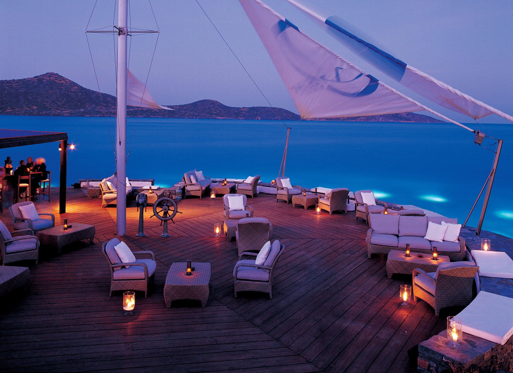 Elounda Beach Hotel And Villas vakara terase ar pītiem atpūtas krēsliem, svecēm un skatu uz Mirabello līci Krētā