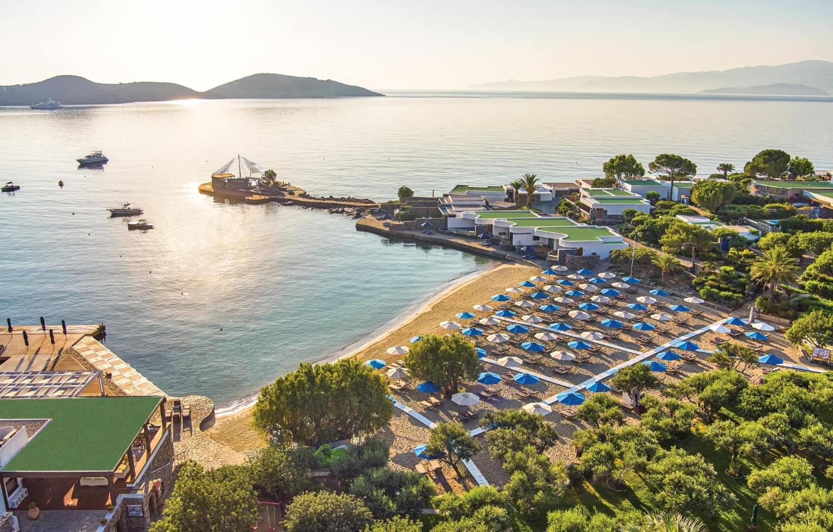 Elounda Beach Hotel And Villas panorāmas skats uz privāto pludmali, saulrietu un kūrorta villām piekrastē