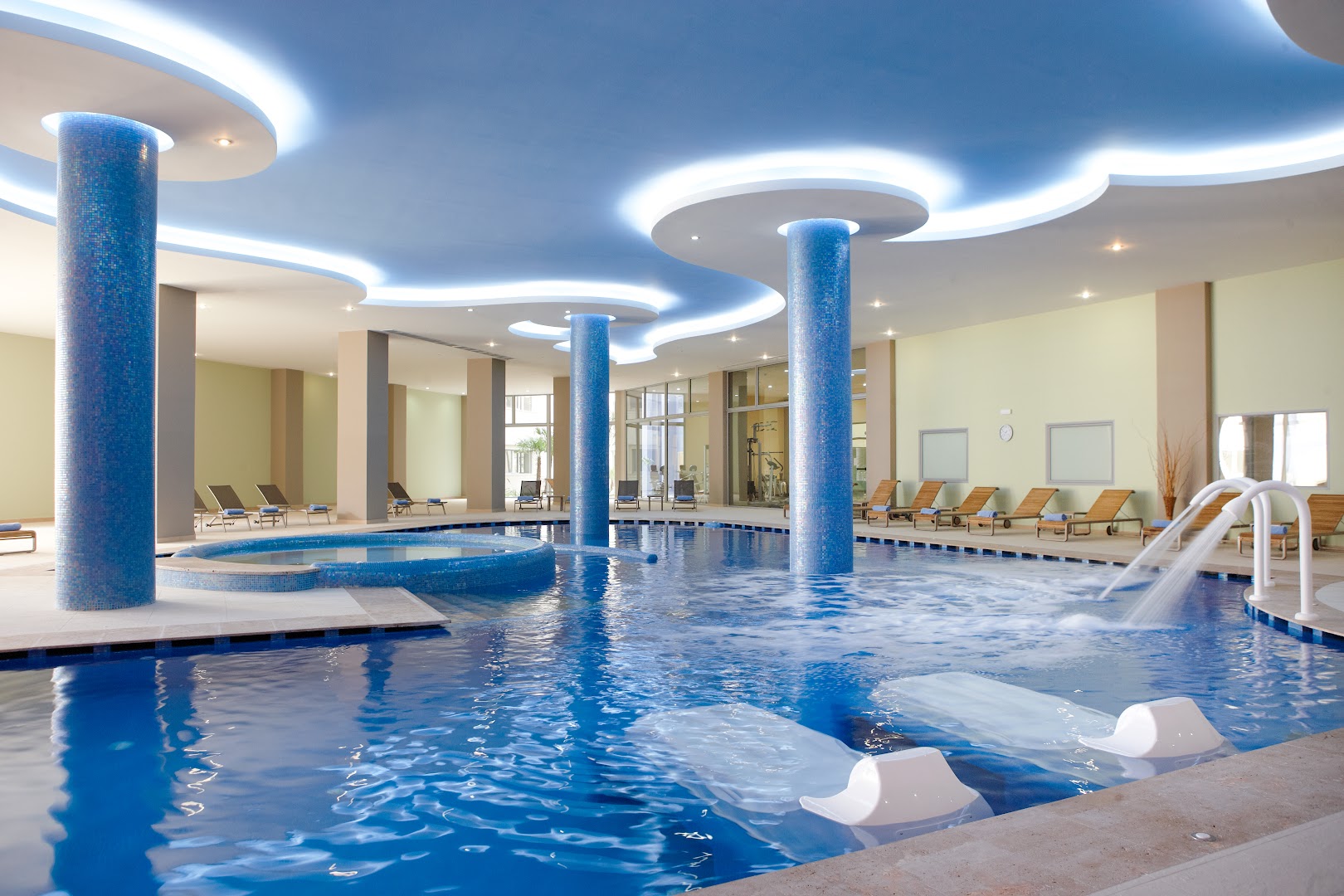 Atrium Platinum viesnīcas iekštelpu spa baseins ar masāžas strūklām, ziliem mozaīkas pīlāriem un modernu griestu apgaismojumu