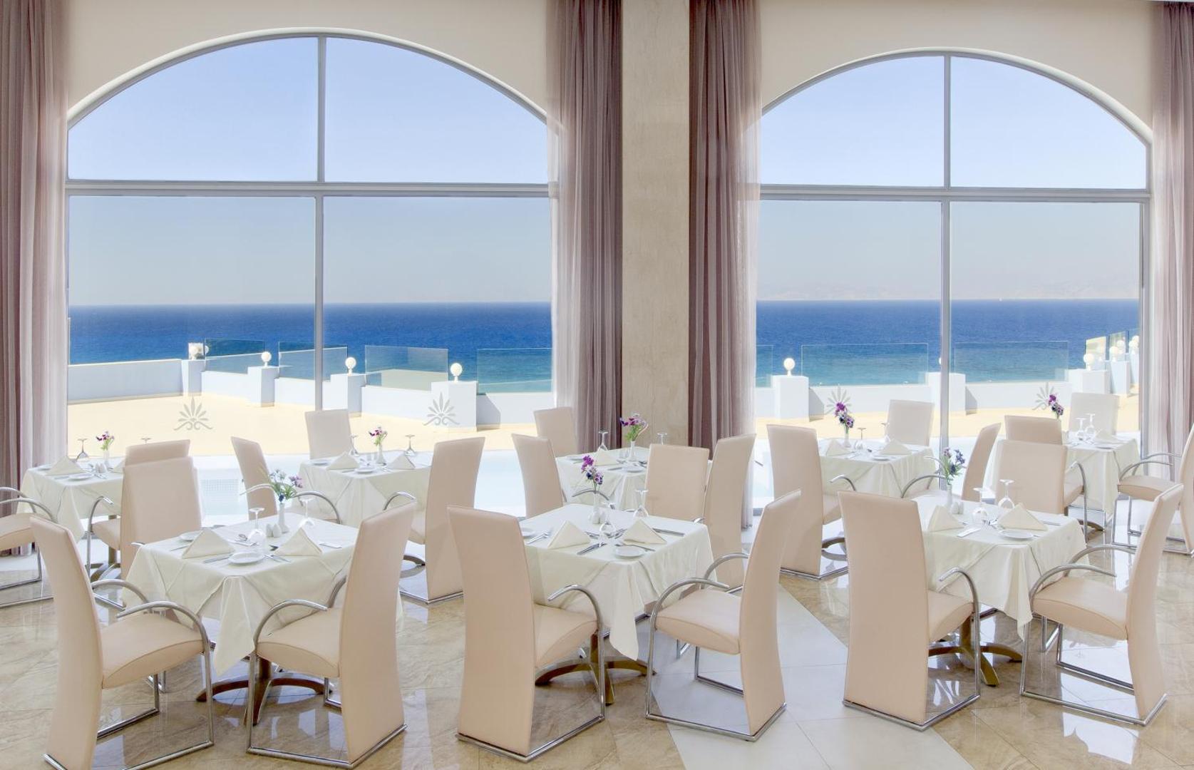 Atrium Platinum Luxury Resort Hotel & Spa gaišais restorāns ar lieliem arkveida logiem un skatu uz Egejas jūru Rodā.