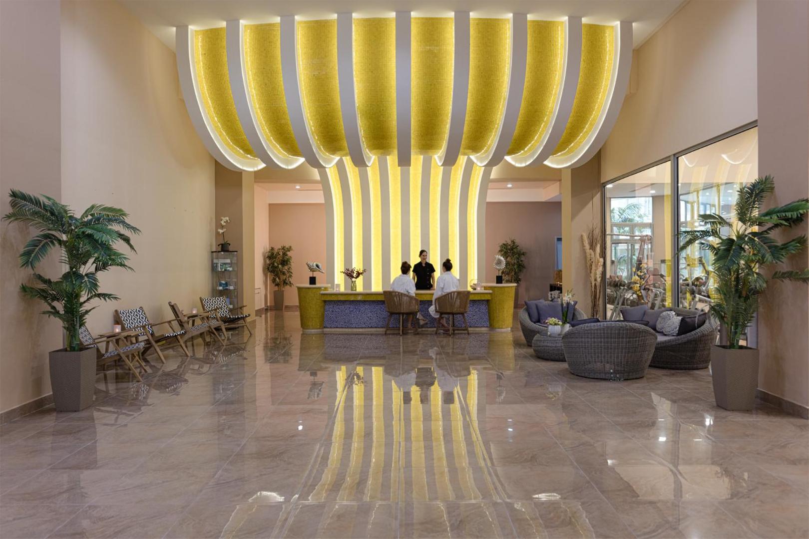 Atrium Platinum Luxury Resort Hotel & Spa modernā spa centra recepcija ar dzeltenu mozaīkas sienu un atpūtas krēsliem.