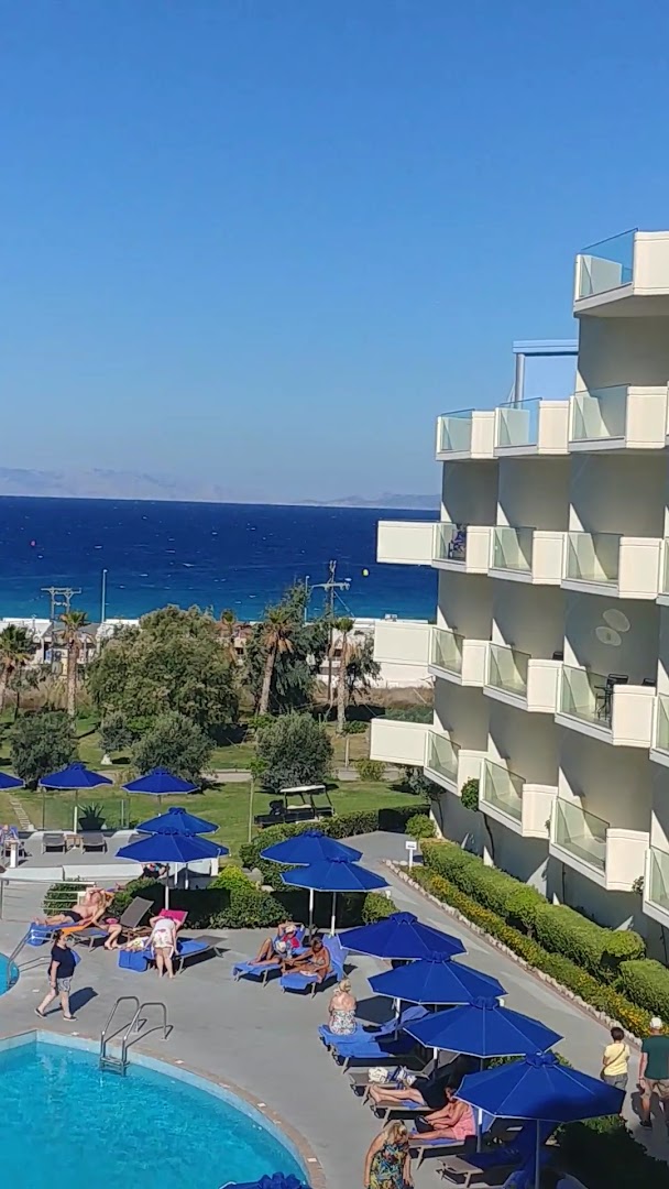 Atrium Platinum viesnīcas korpuss ar balkoniem un atpūtas zonu pie baseina zem ziliem saulessargiem Rodā