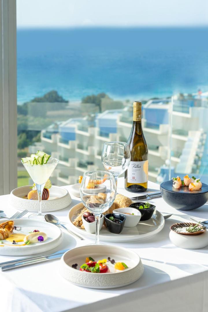Gourmet vakariņas Atrium Platinum restorānā ar skatu uz Egejas jūru — eleganti servēts galds ar vīnu un uzkodām