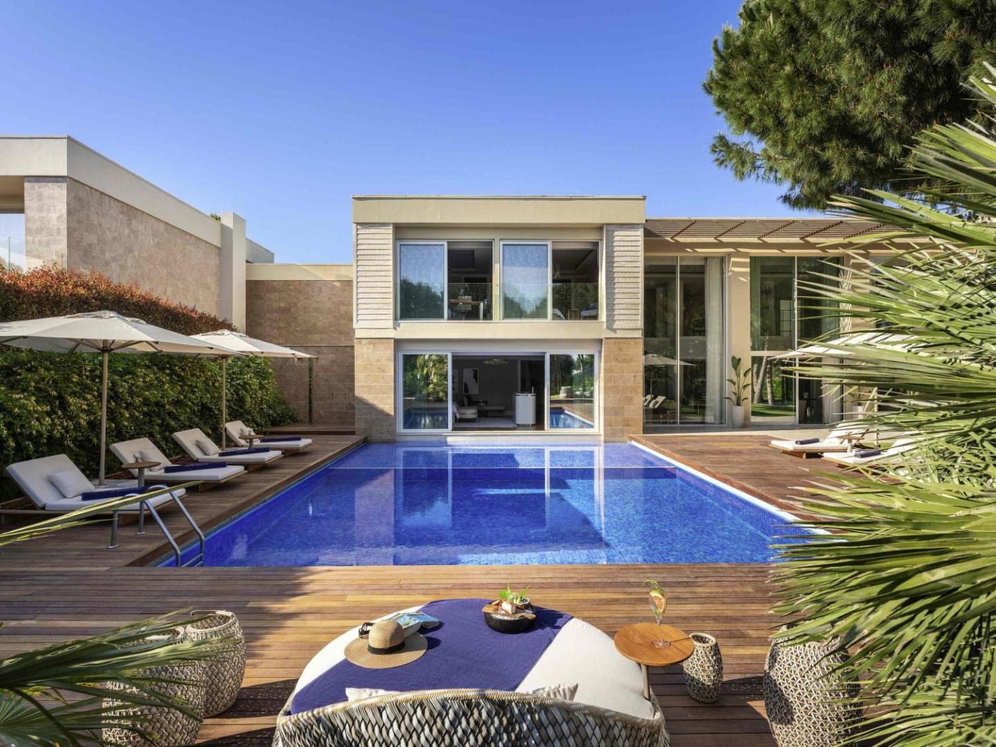 Rixos Premium Belek modernas divstāvu villas eksterjers ar privātu baseinu, koka klāju un komfortabliem zviļņiem saulainā dienā