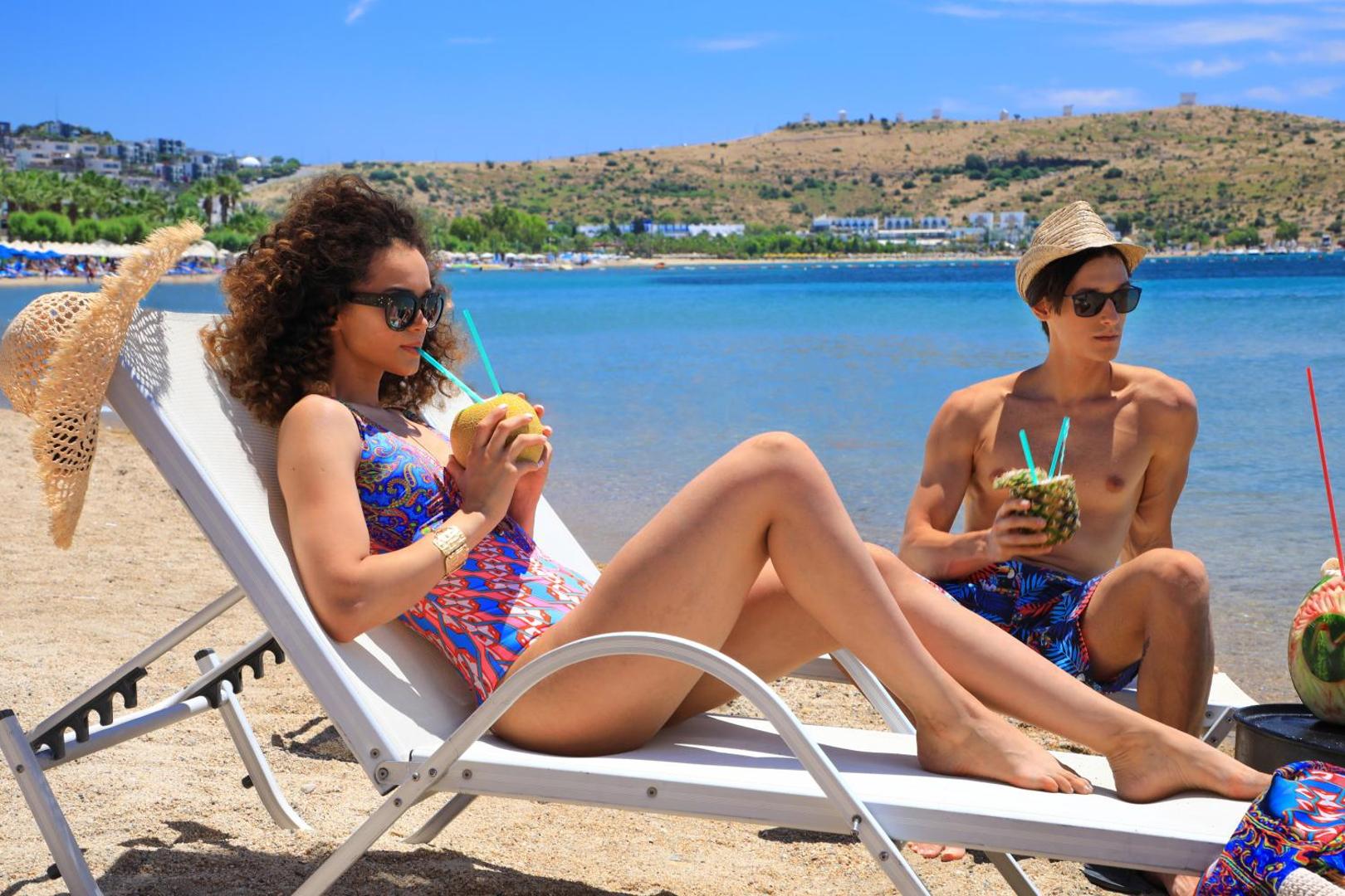 Atpūtnieki pludmales zviļņos Otium Senses Very Chic Bodrum kūrortā Bodrumā — eksotiski kokteiļi un skats uz līci