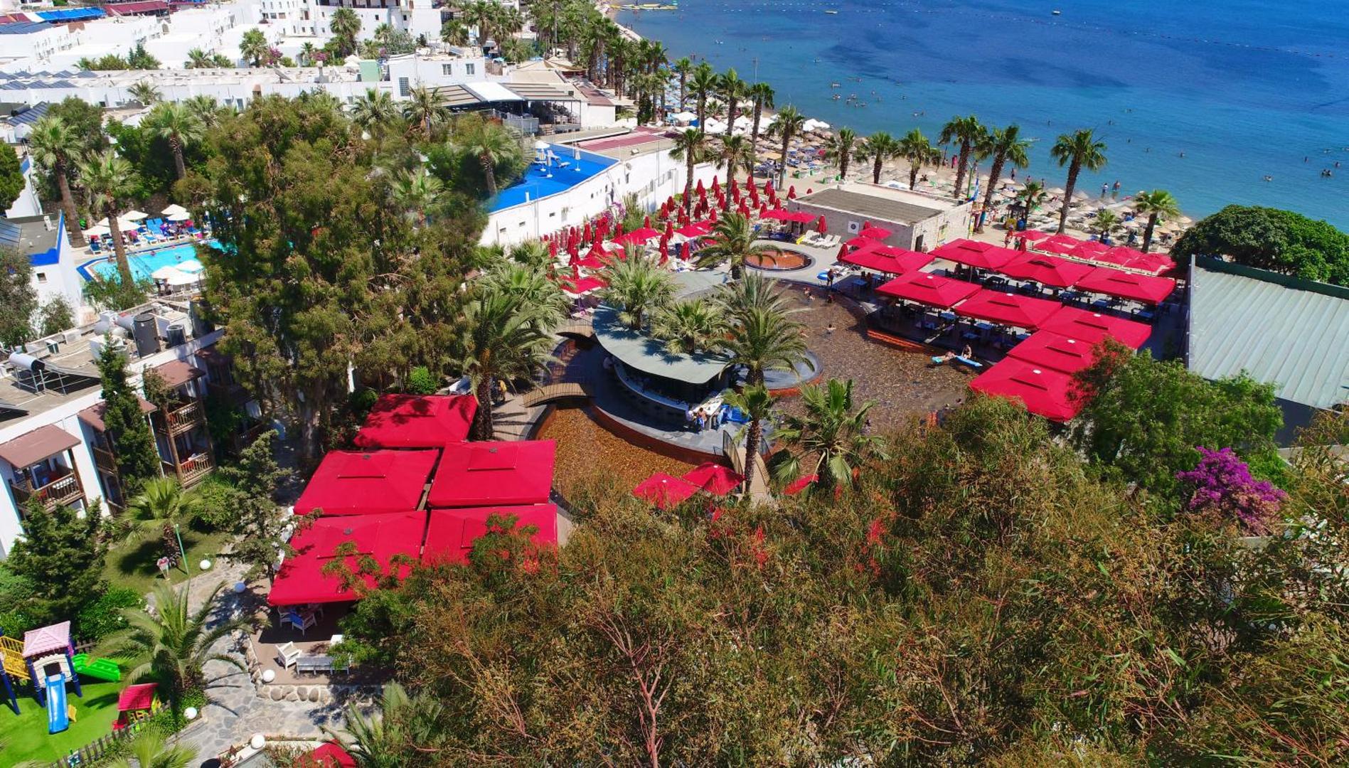 Otium Senses Very Chic Bodrum skats no augšas uz baseina zonu ar sarkaniem saulessargiem un blakus esošo pludmali Gumbetā