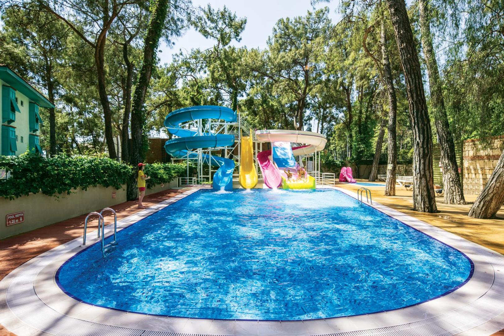 Ulusoy Kemer Holiday Club āra baseins ar krāsainiem ūdens slidkalniņiem priežu meža ieskautā teritorijā Kemeras reģionā, Turcijā