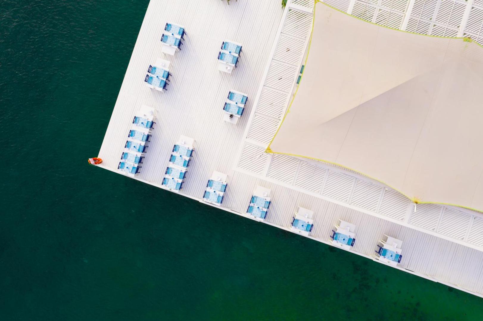 La Blanche Resort & Spa restorāna terase no putna lidojuma skata Turgutreisā, Bodrumā — balti galdi ar ziliem akcentiem virs tirkīzzila ūdens