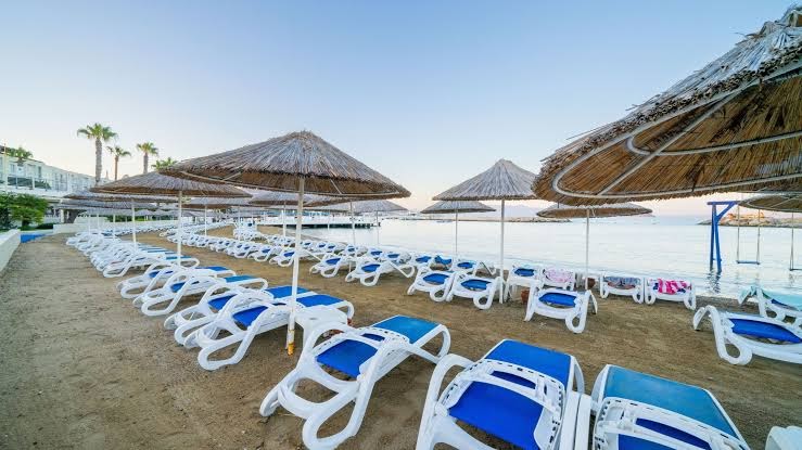La Blanche Resort & Spa privātā pludmale ar saulessargiem un sauļošanās krēsliem Bodrumā — smilšaina piekraste un mierīga jūra