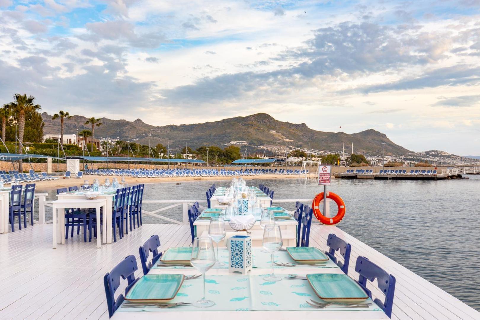 La Blanche Resort & Spa restorāna terase uz koka platformas virs ūdens ar klātiem galdiem un skatu uz kalniem