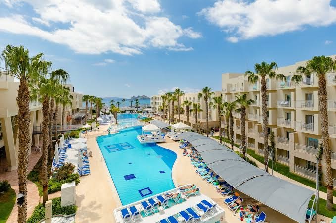 La Blanche Resort & Spa plašā teritorija ar lielu āra baseinu, palmām un viesnīcas korpusiem Turgutreisā, Bodrumas reģionā