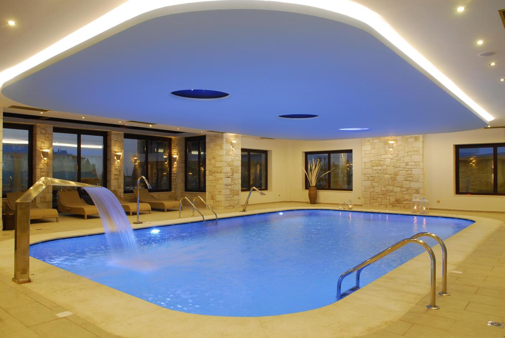 Iekštelpu spa baseins ar kaskādi, silto apgaismojumu un atpūtas krēsliem.