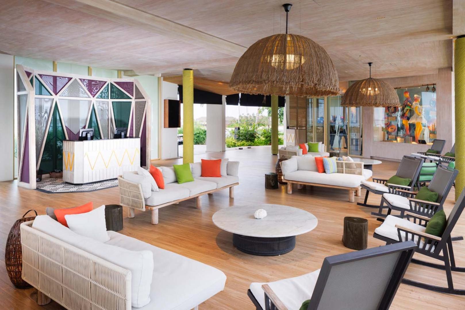 Hard Rock Hotel Maldives plašais vestibils ar modernām mēbelēm, košiem spilveniem un stilīgiem gaismekļiem — atpūtas zona viesu uzņemšanai