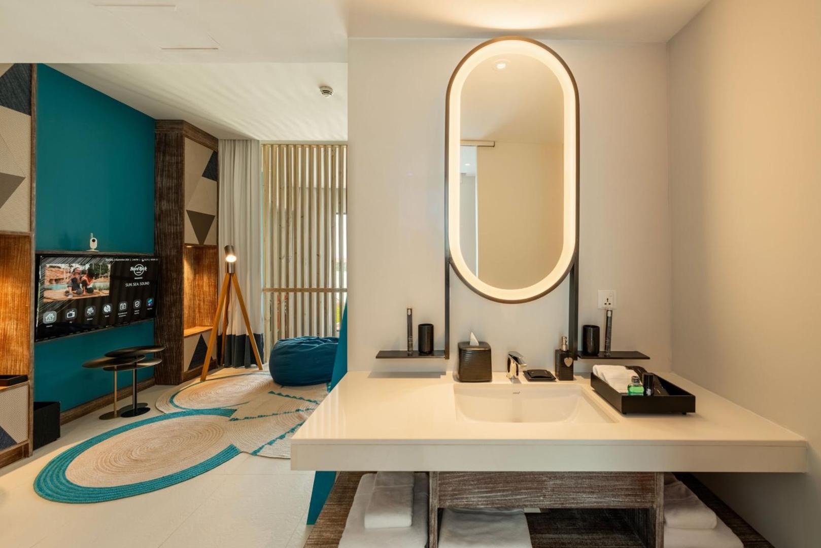 Hard Rock Hotel Maldives dizaina numura interjers ar modernu izlietni, izgaismotu spoguli un atpūtas zonu fonā