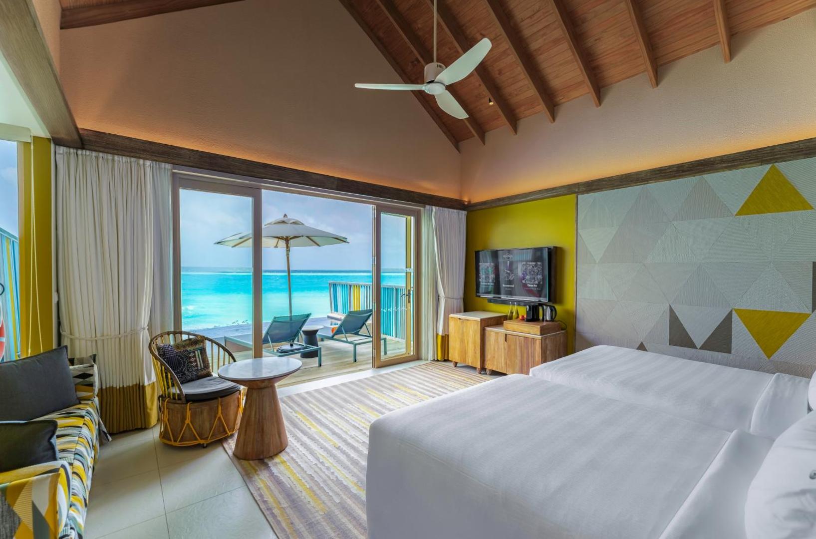 Hard Rock Hotel Maldives gaišs numurs ar divām gultām, koka griestiem un terasi, no kuras paveras skats uz tirkīzzilo okeānu.